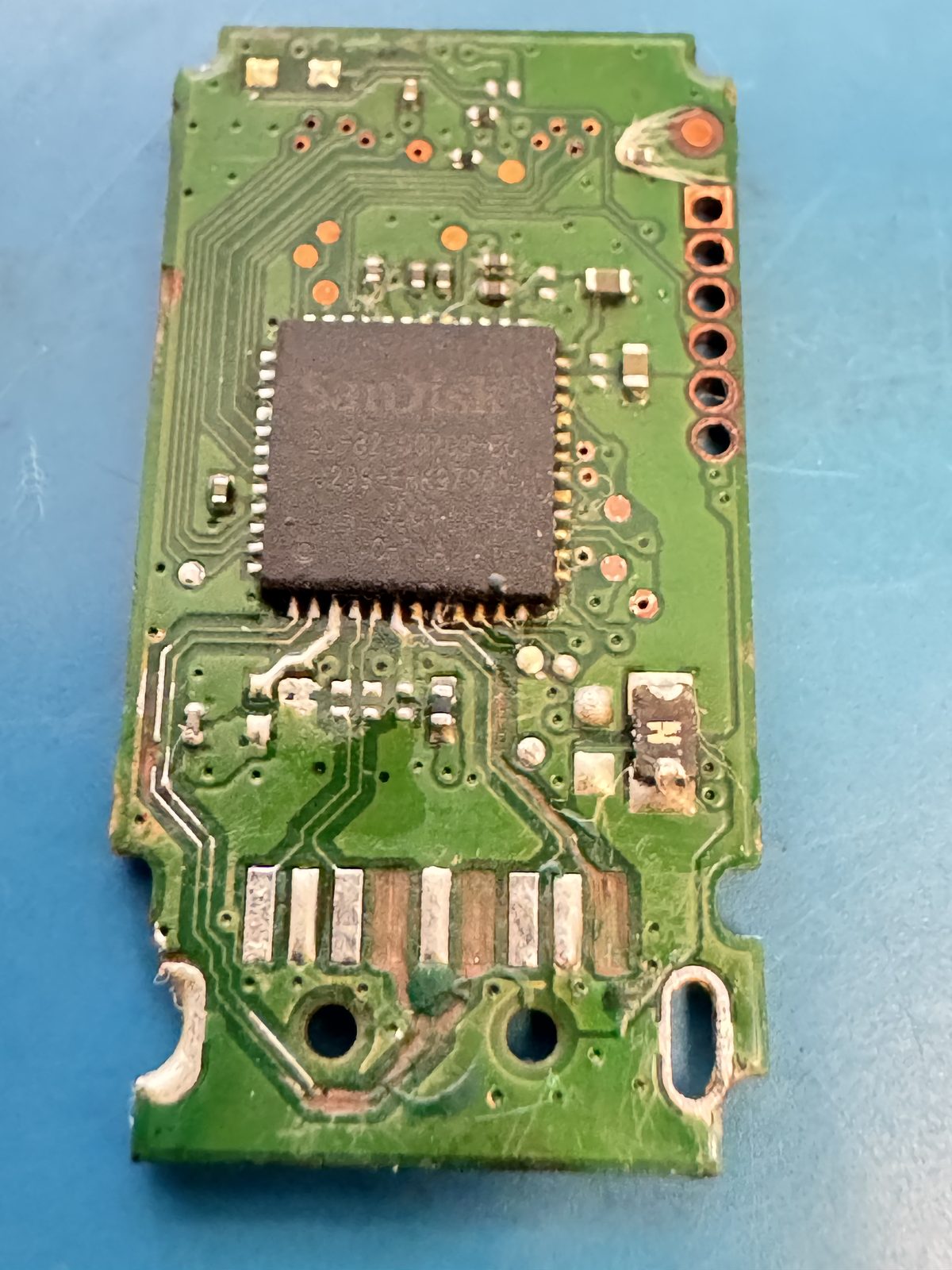 The SanDisk Ultra USB 3.0 flash drive board, with the controller marked 20-82-00709-B0 at centre and visible damage to the pads and traces around the USB contacts